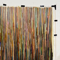 Multicolored fabric strips hanging vertically on a white wall.