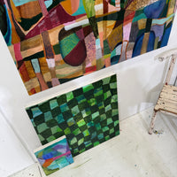 Colorful abstract artwork on a white wall with a green checkered piece of fabric on a table below.